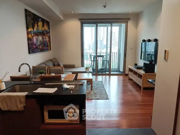 Modern living room with open kitchen and balcony view, featuring sleek furniture and wooden flooring.