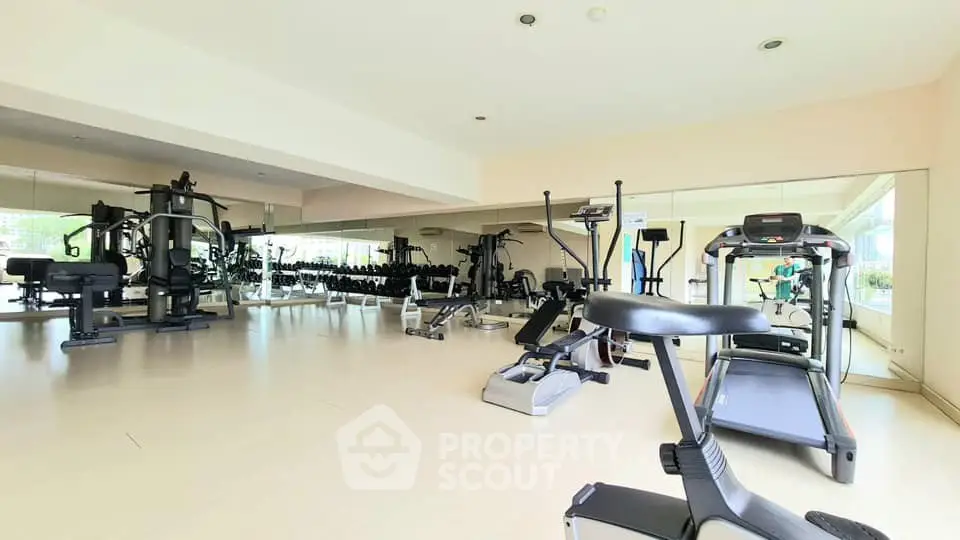 Spacious gym with modern fitness equipment and mirrored walls in a luxury apartment building.