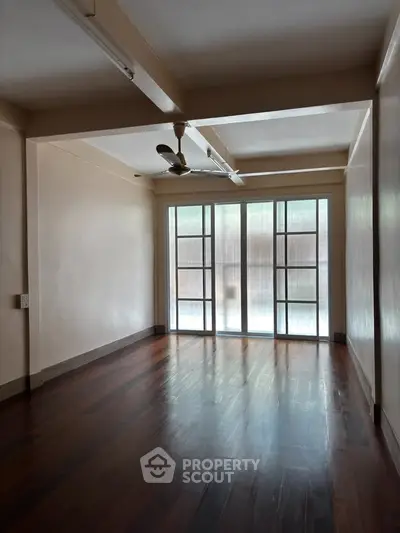 Spacious empty room with wooden flooring and large windows, ideal for customization.