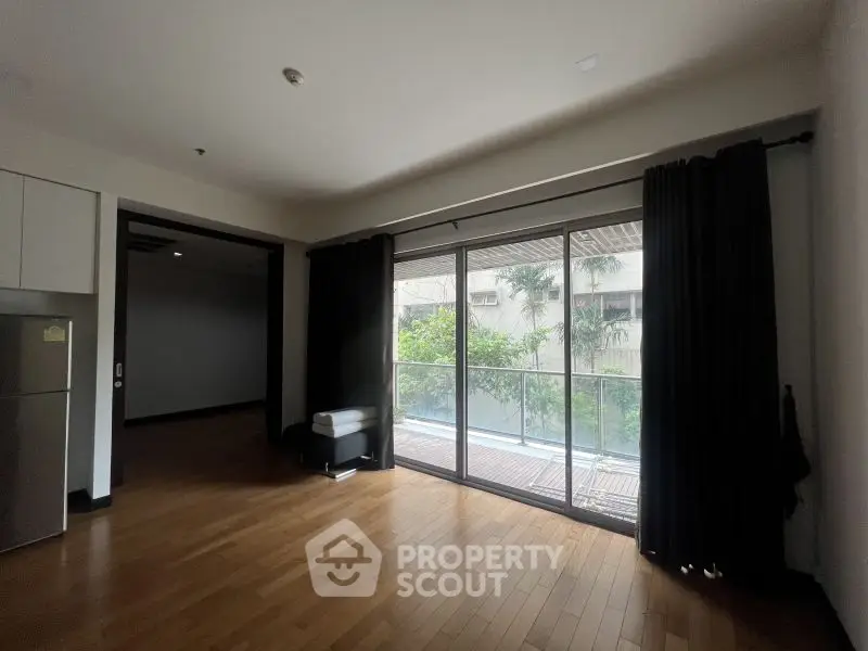 Spacious living room with large windows and balcony view, featuring hardwood floors and modern design.