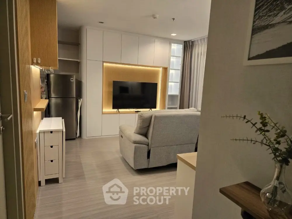 Modern living room with sleek design and integrated kitchen area, featuring a cozy sofa and large TV.
