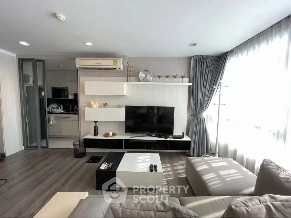 Modern living room with sleek furniture and open kitchen layout, featuring ample natural light and stylish decor.