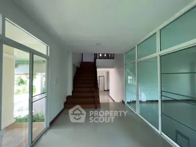 Spacious modern hallway with glass partitions and wooden staircase in a contemporary home.