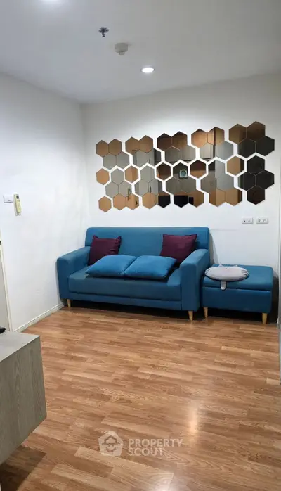 Modern living room with stylish blue sofa and hexagonal mirror decor on wooden floor.