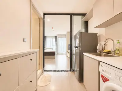 Modern apartment kitchen with sleek appliances and view into cozy bedroom