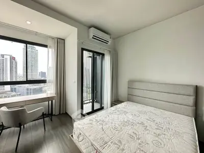 Modern bedroom with city view, featuring a cozy bed, desk, and balcony access in a high-rise apartment.