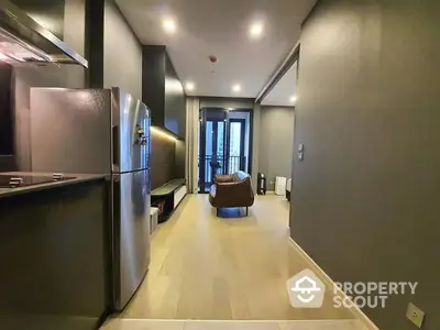 Modern kitchen with stainless steel appliances flows into a cozy living area with balcony access, featuring sleek finishes and a warm ambiance.