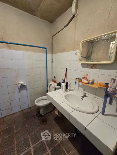 Modest bathroom with basic fixtures and tiled walls, featuring a sink, toilet, and mirror.