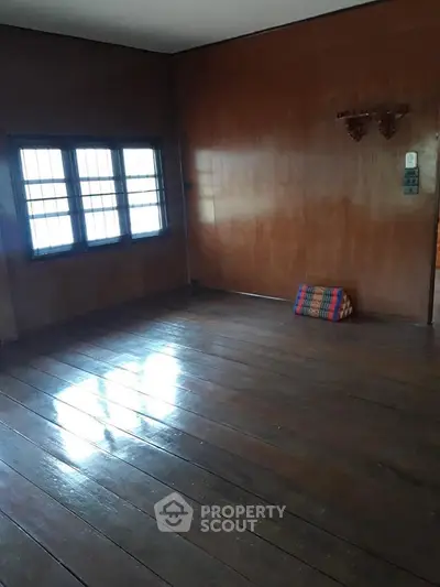 Spacious empty room with wooden floors and large window, perfect for customization.