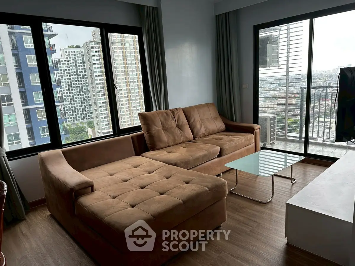 Spacious living room with large windows and city view, featuring a cozy brown sectional sofa.