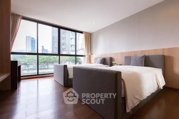 Spacious modern bedroom with twin beds and large windows offering city view.