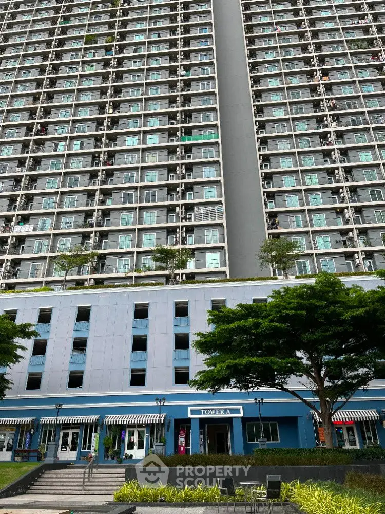 Modern high-rise residential building with lush greenery and retail shops at the base.