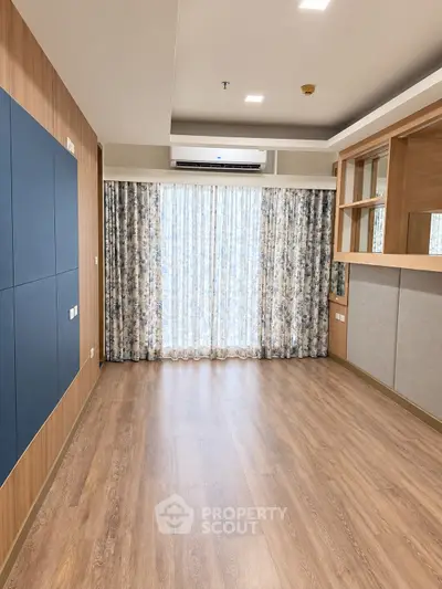 Spacious empty room with wooden flooring and large window with floral curtains, ideal for customization.