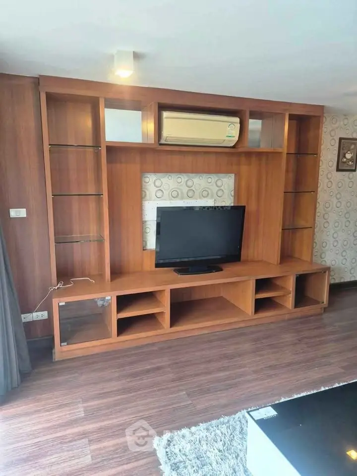 Modern living room with wooden entertainment center and flat-screen TV, featuring stylish decor and air conditioning.