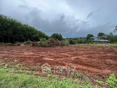 Expansive plot of land with lush greenery and modern house in the background, ideal for development.