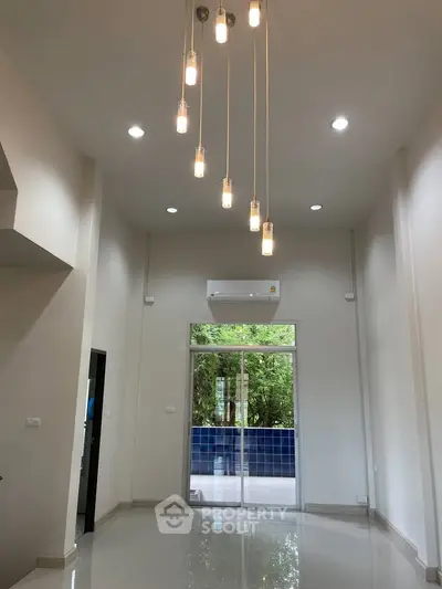 Modern living room with high ceiling and stylish lighting, overlooking a lush garden.