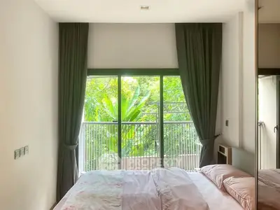 Bright bedroom with large window and lush garden view, featuring elegant curtains and cozy bedding.