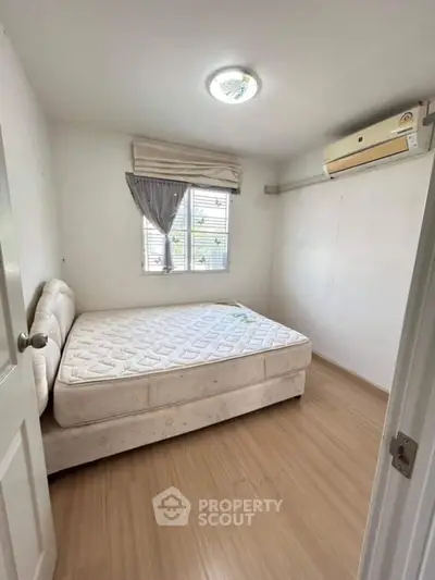 Cozy bedroom with natural light and air conditioning, featuring a comfortable bed and wooden flooring.