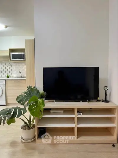 Modern living room with TV stand and kitchen view, featuring sleek wooden furniture and potted plant.