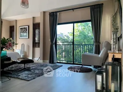 Stylish living room with large window and cozy seating area overlooking lush greenery.