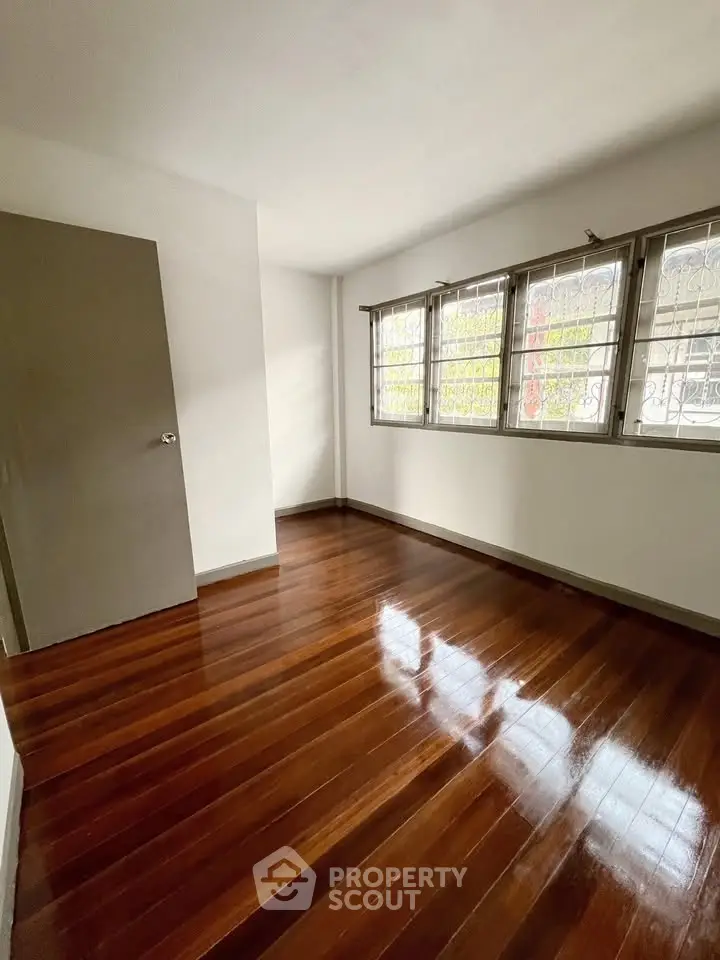 Spacious bedroom with polished wooden floors and large windows for natural light.