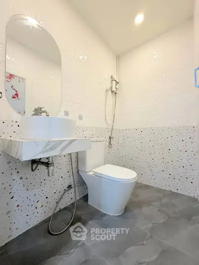 Modern bathroom with sleek fixtures and terrazzo tiles, featuring a stylish mirror and efficient lighting.