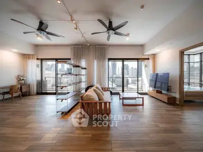 Spacious modern living room with large windows and city view, featuring stylish furniture and wooden flooring.