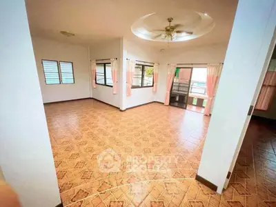 Spacious living room with tiled flooring and ceiling fan, featuring large windows and natural light.