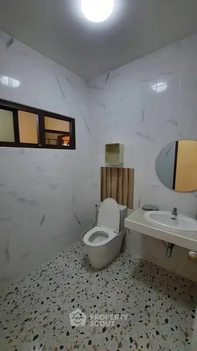 Modern bathroom with sleek design and terrazzo flooring, featuring a round mirror and contemporary fixtures.