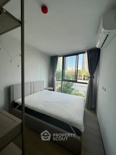 Modern bedroom with large window and city view, featuring a comfortable bed and air conditioning.