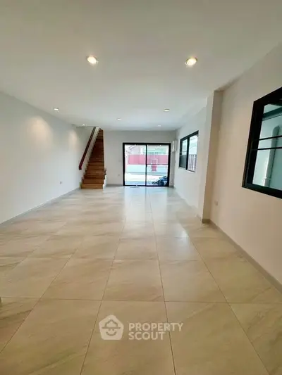 Spacious open-plan living room with modern tile flooring and staircase, perfect for family gatherings.