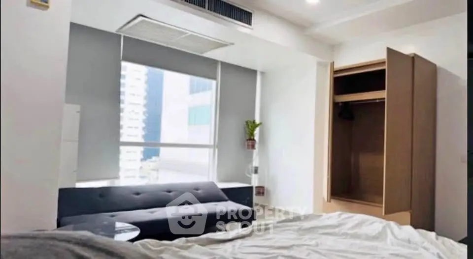 Modern bedroom with large window, sleek sofa, and open wardrobe in a high-rise apartment.