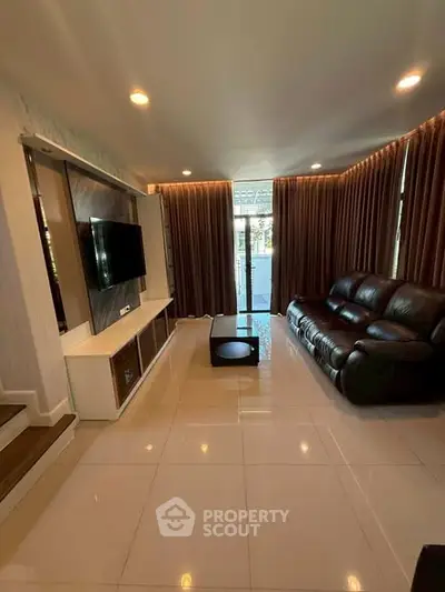 Spacious modern living room with sleek leather sofa and large TV, perfect for relaxation.