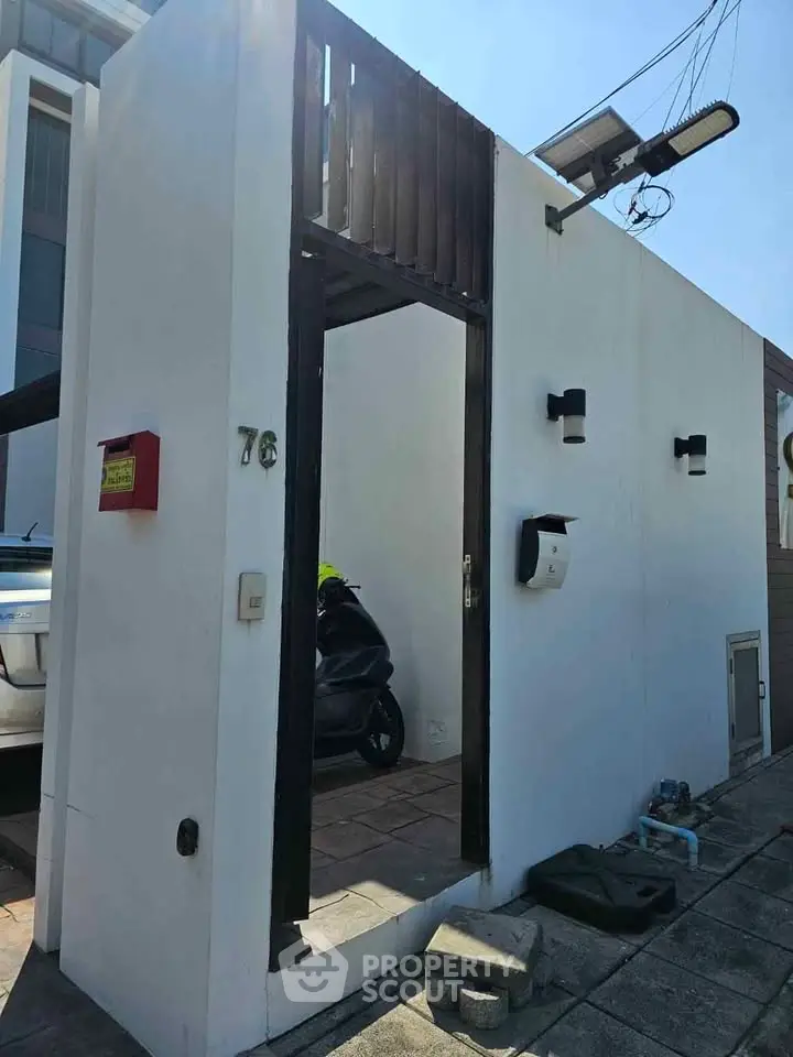 Modern minimalist exterior with sleek white walls and stylish lighting, featuring a secure entrance and scooter parking.