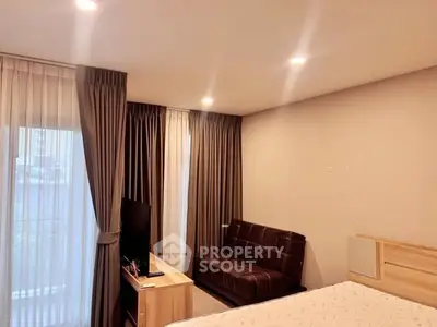 Cozy bedroom with modern decor and natural light, featuring a stylish sofa and TV setup.
