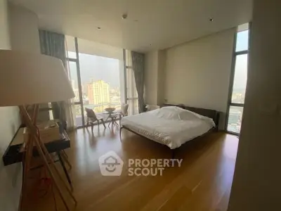 Spacious bedroom with floor-to-ceiling windows offering stunning city views and modern furnishings.