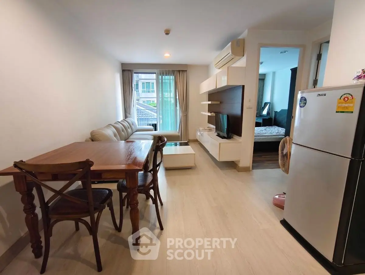 Modern apartment living room with dining area and view into bedroom, featuring sleek furniture and natural light.