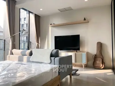 Modern bedroom with large windows, stylish furniture, and natural light in a high-rise apartment.