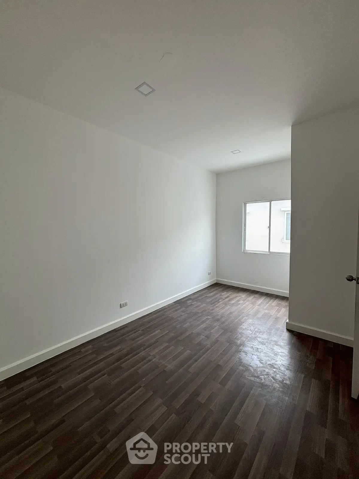 Spacious empty room with wooden flooring and natural light from window.
