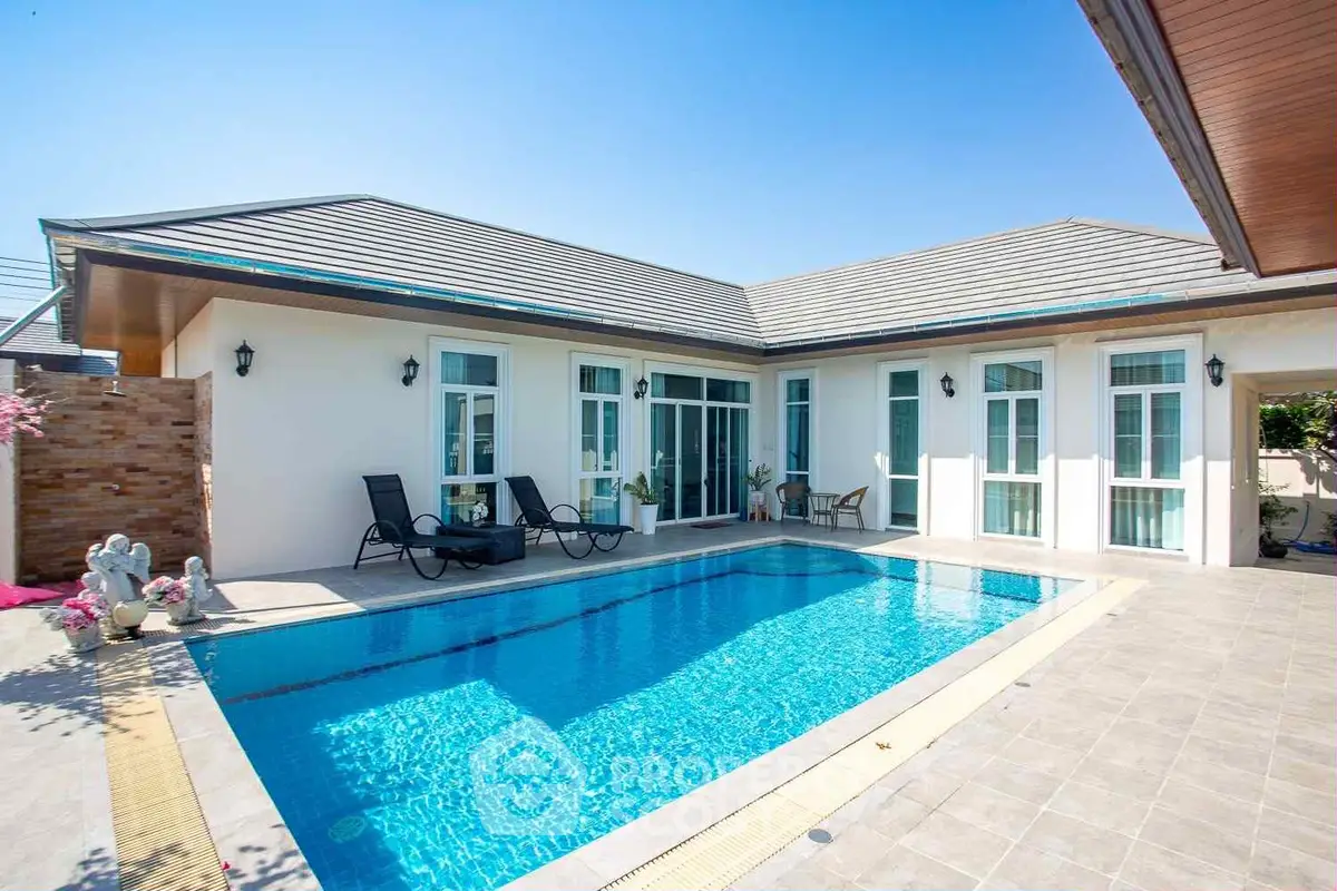 Luxurious villa with private pool and sun loungers under clear blue sky.