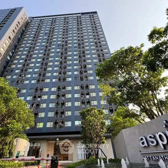 Modern high-rise building with lush greenery and clear blue sky.