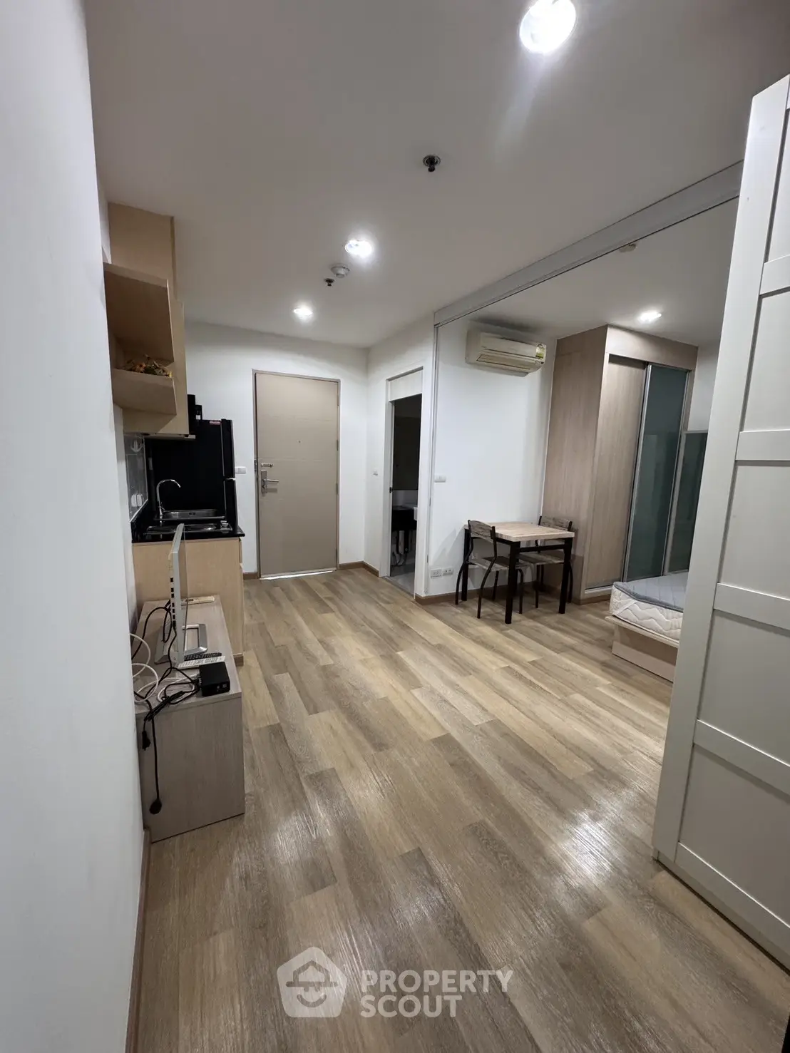 Modern studio apartment with wooden flooring and compact kitchen in open layout.