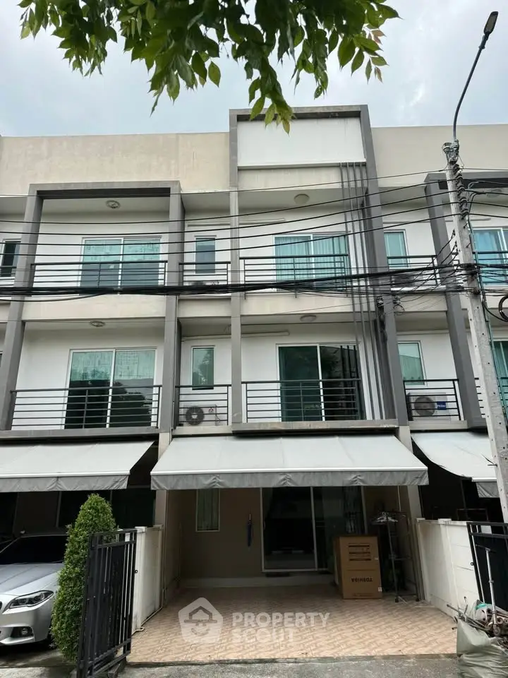 Modern townhouse exterior with three floors and balconies, featuring a sleek design and ample parking space.