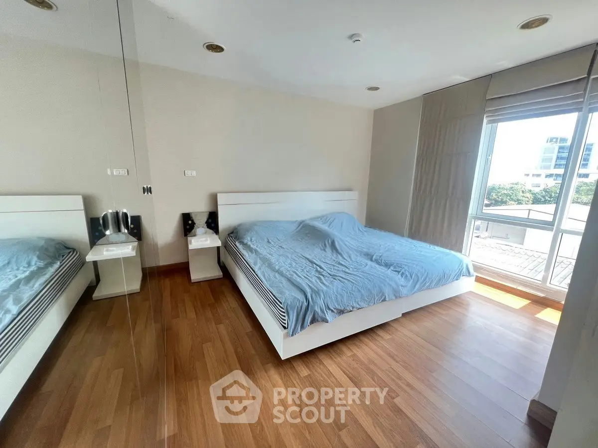 Spacious bedroom with large window and wooden flooring in modern apartment