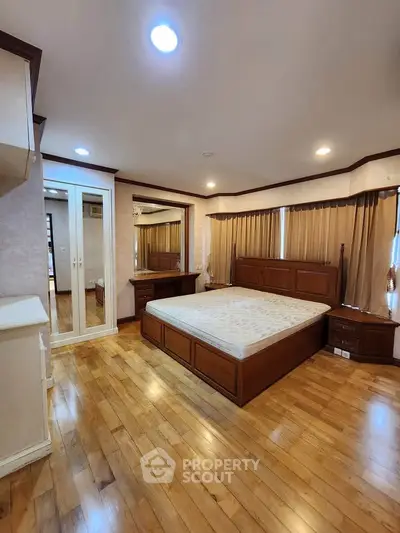 Spacious bedroom with wooden flooring and elegant furnishings in a modern apartment.