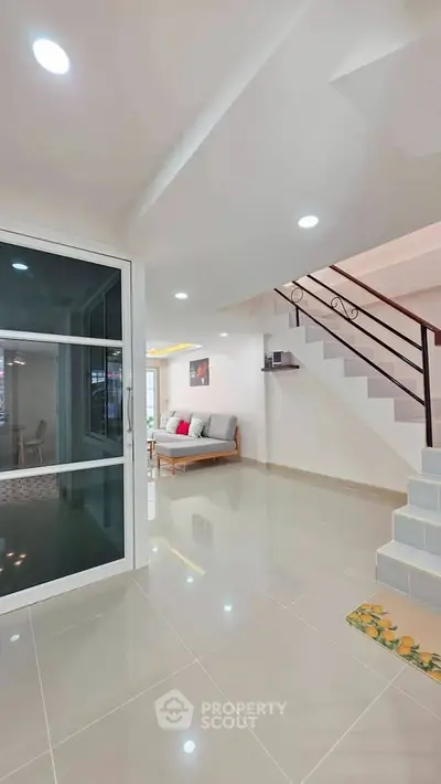 Modern living room with staircase and glass door, featuring sleek design and bright lighting.