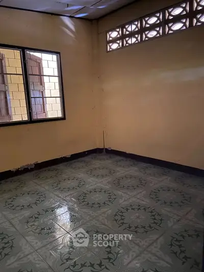 Spacious empty room with patterned tile flooring and natural light from windows.