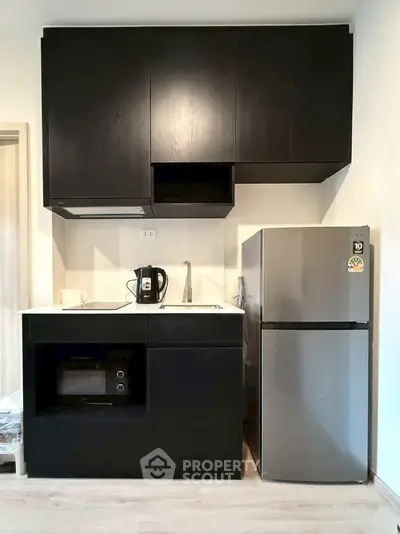 Modern compact kitchen with sleek black cabinets and stainless steel fridge