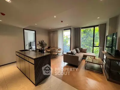 Modern open-plan living room with stylish kitchen island and large windows overlooking greenery.