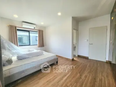 Spacious bedroom with modern design and natural light, featuring hardwood floors and a large window.